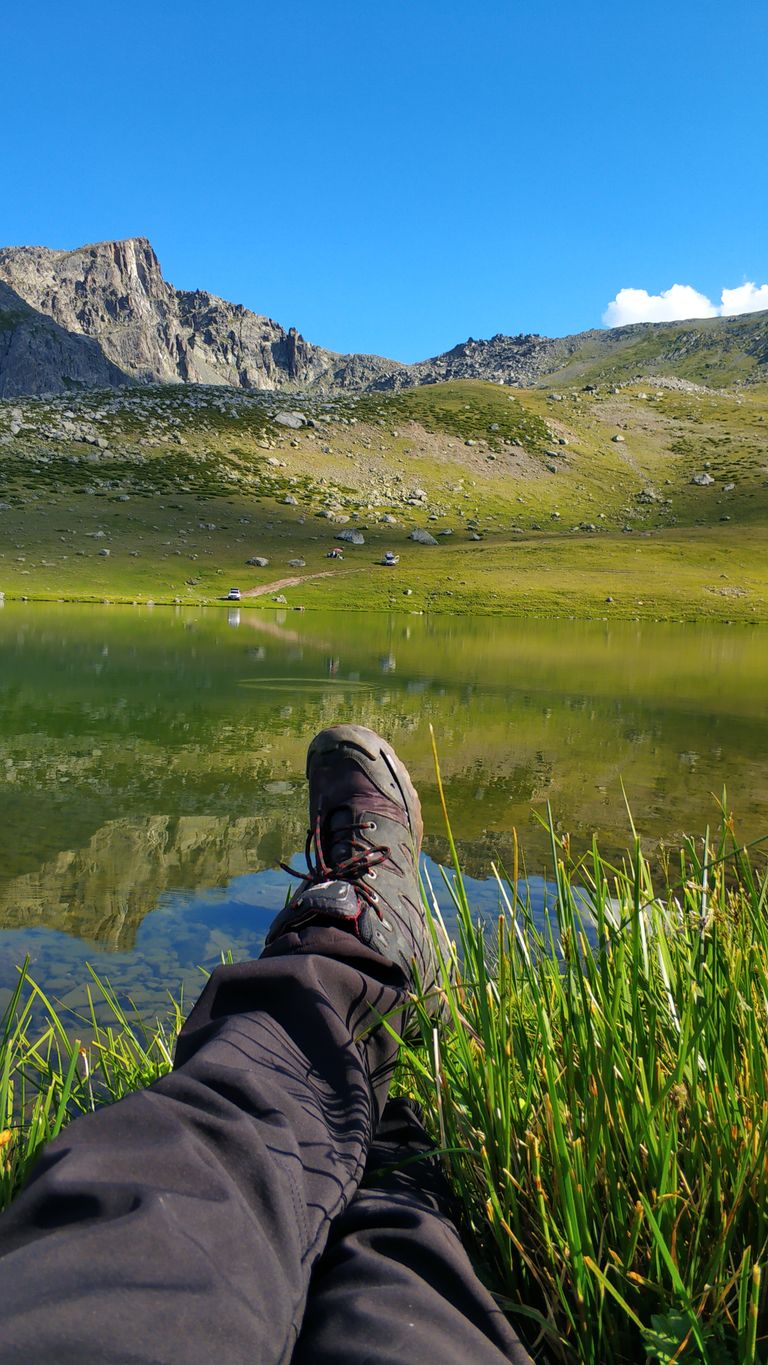 A hiker relaxes by a tranquil mountain lake under a clear blue sky.